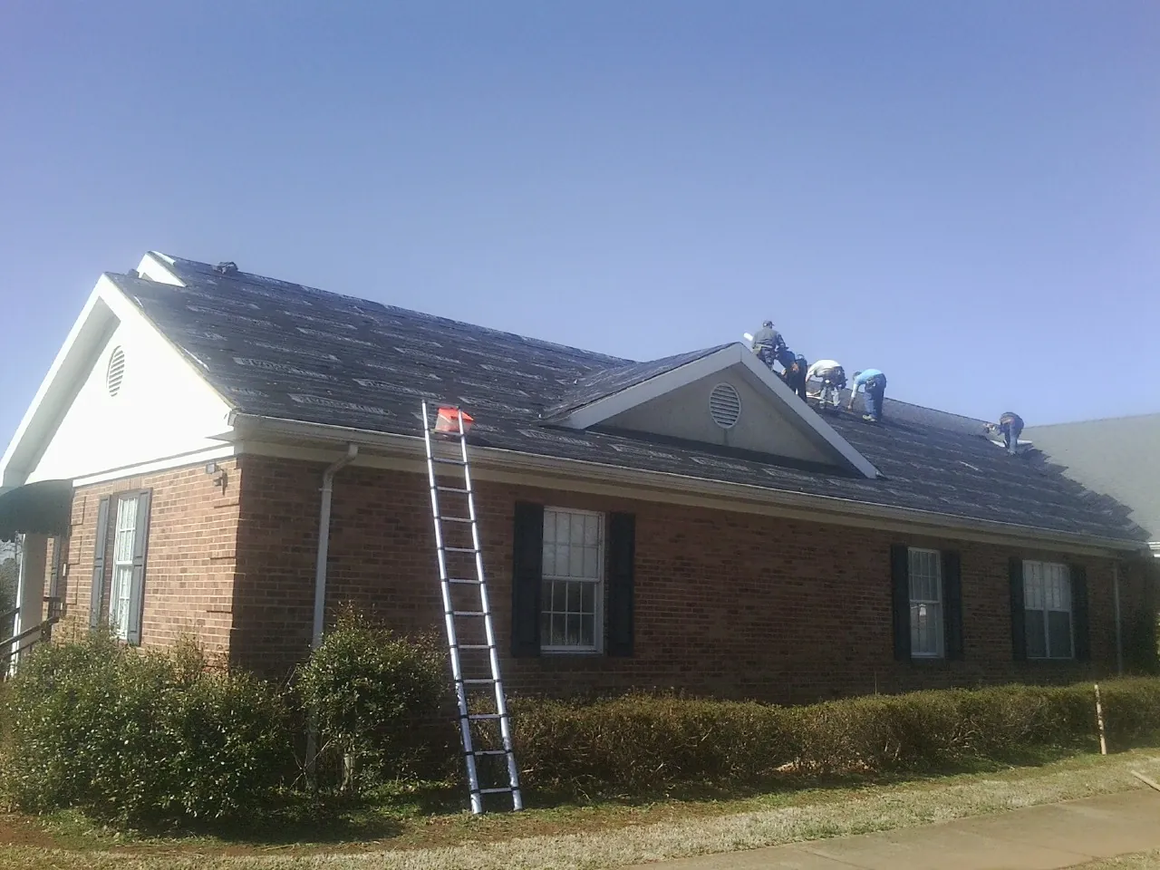 Crew tearing shingles off a brick ranch roof with a ladder set — Emergency Roof Repair work by our crew in Canyon Lake