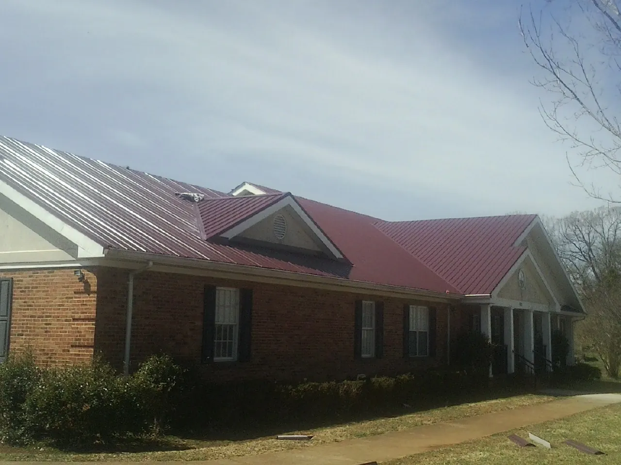 Red metal roof with gabled entries on a long brick building, from a Hail Damage Roof Repair job in Canyon Lake