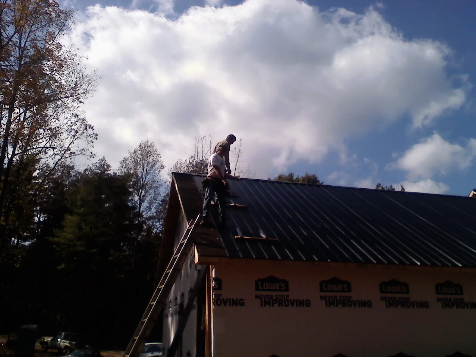 Roofer fastening dark metal panels high against a cloudy sky, from a Roof Inspection job in Canyon Lake