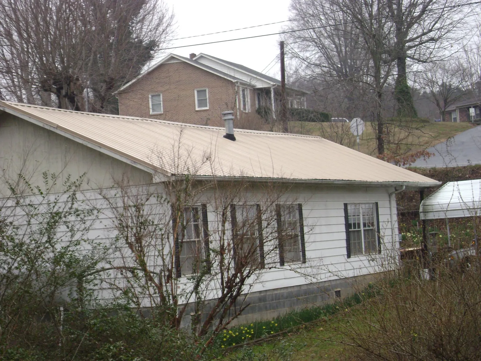 Tan metal roof on a white sided house set into a hillside — Commercial Roofing by Roofing Brothers in Canyon Lake