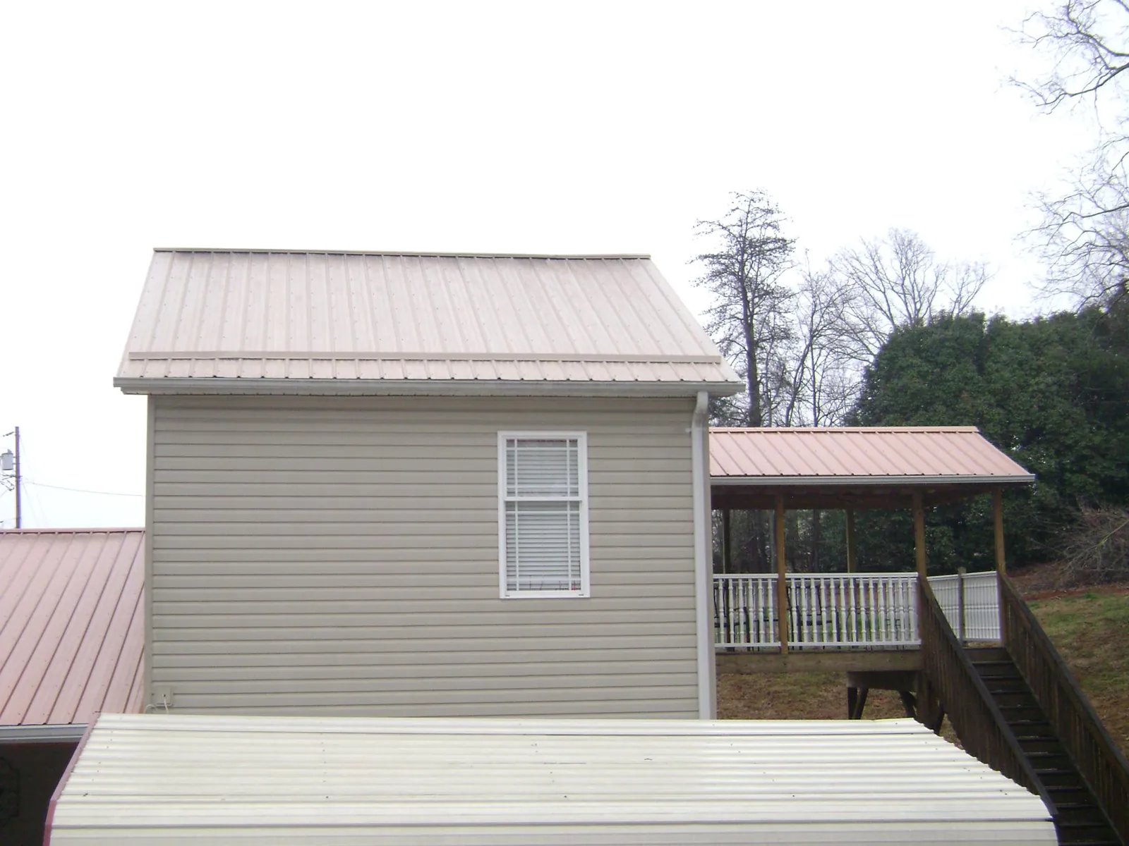 Tan metal roofs on a two story addition and attached porch, from a Roof Replacement job in Canyon Lake